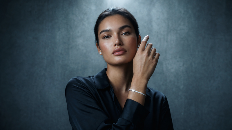 Woman in a dark shirt raising her hand to show a diamond tennis bracelet
