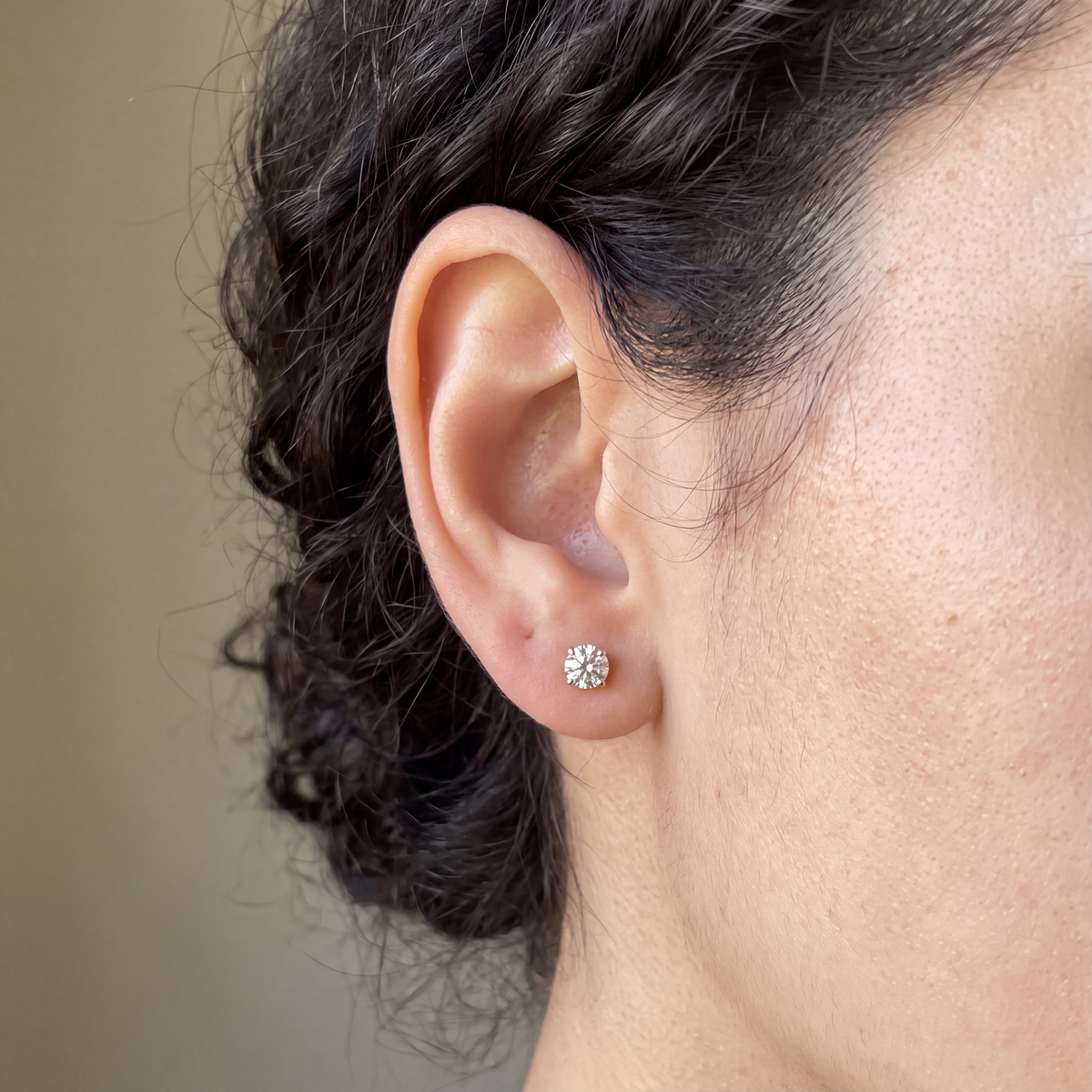 Candid-style close-up of one of a pair of 1 carat lab-grown diamond stud earrings in 14K yellow gold, worn on the ear, AI-generated image — DEEVE