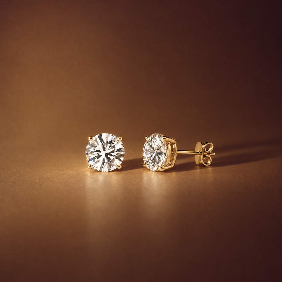Pair of 2 carat round lab-grown diamond stud earrings in 14K yellow gold, one shown side-on with its four-prong basket, post and push back, brown background, AI-generated image — DEEVE