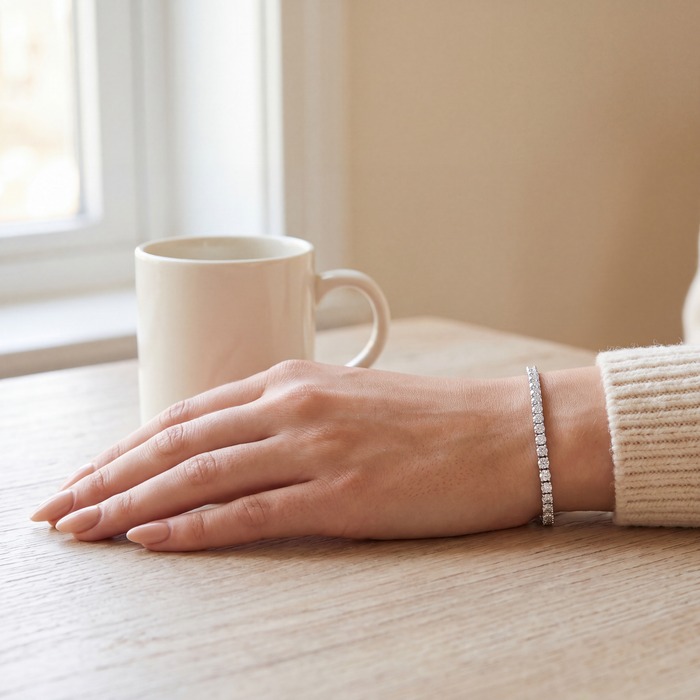 3 carat lab-grown diamond tennis bracelet in 14K white gold worn on the wrist, hand resting on a wooden table beside a mug, AI-generated image — DEEVE