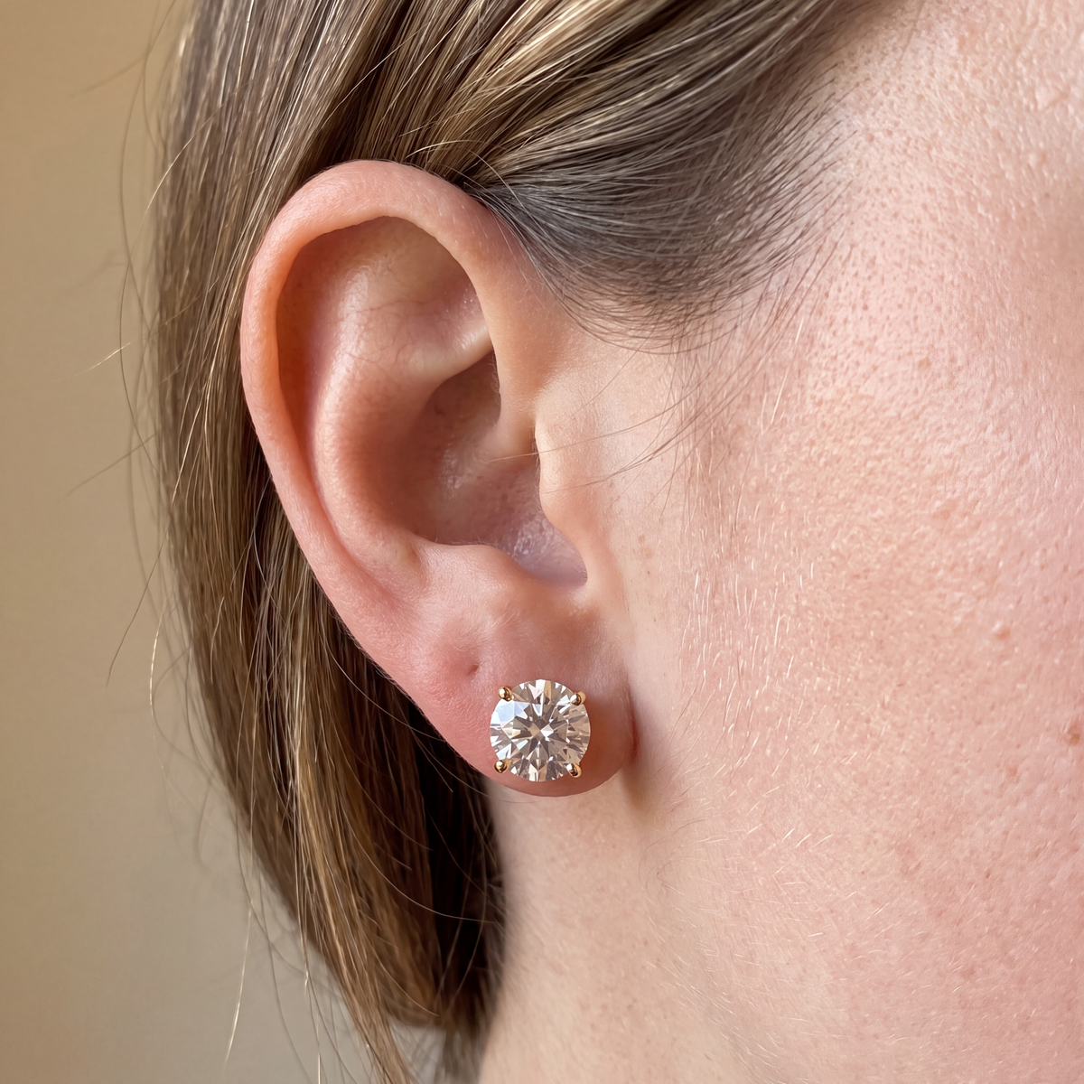 Candid-style close-up of one of a pair of 4 carat lab-grown diamond stud earrings in 14K yellow gold, worn on the ear, AI-generated image — DEEVE