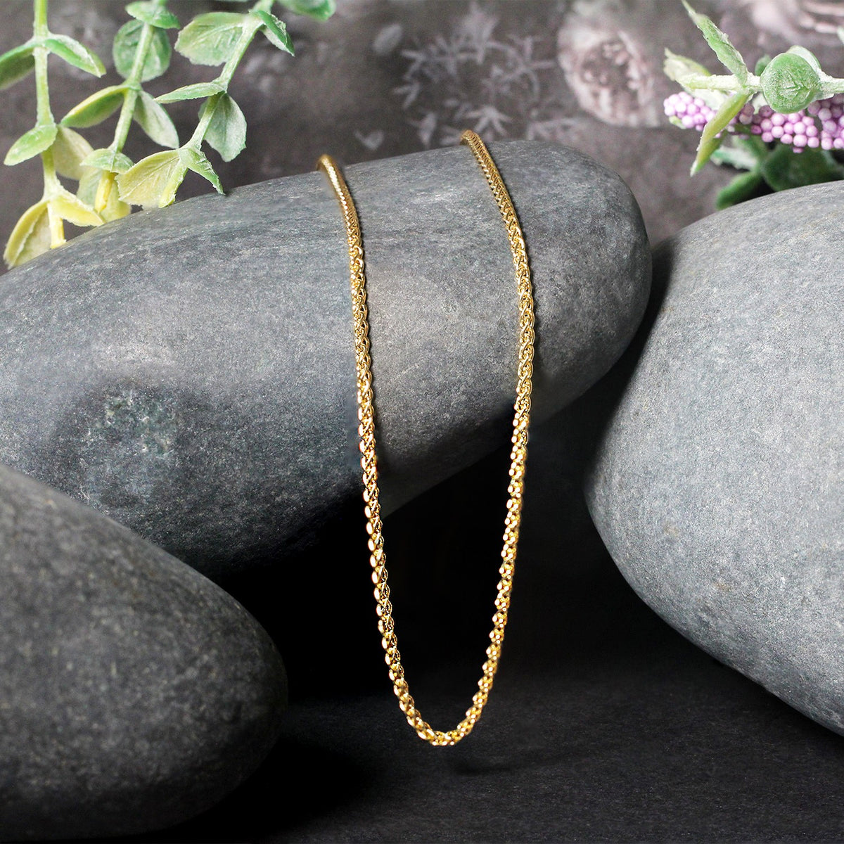 Wheat chain in 14K yellow gold draped over two stones