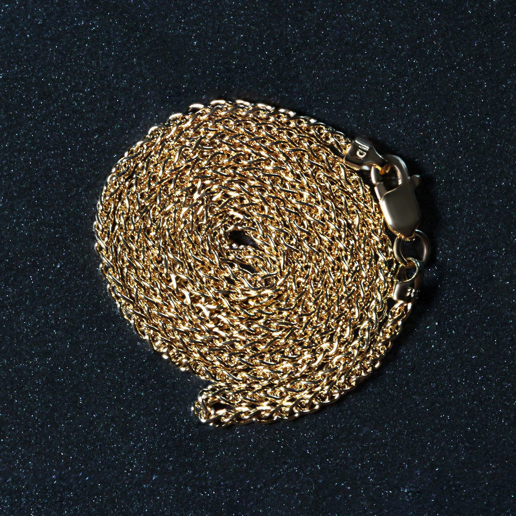 14K yellow gold wheat chain, 1.5mm, coiled on a dark surface