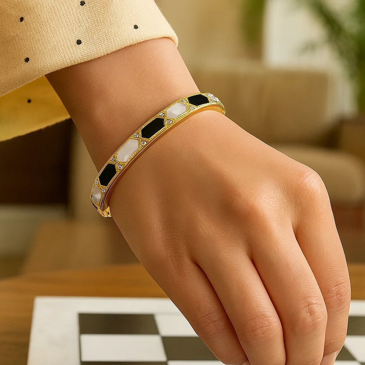 14K yellow gold onyx and mother-of-pearl bangle worn on the wrist beside a chess piece