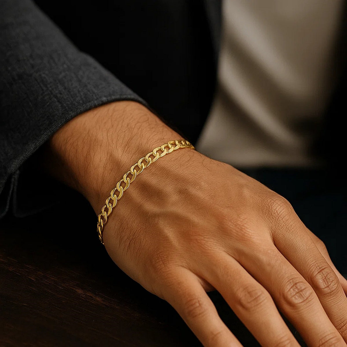 Curb bracelet in 14K yellow gold on a man's hand resting on dark wood