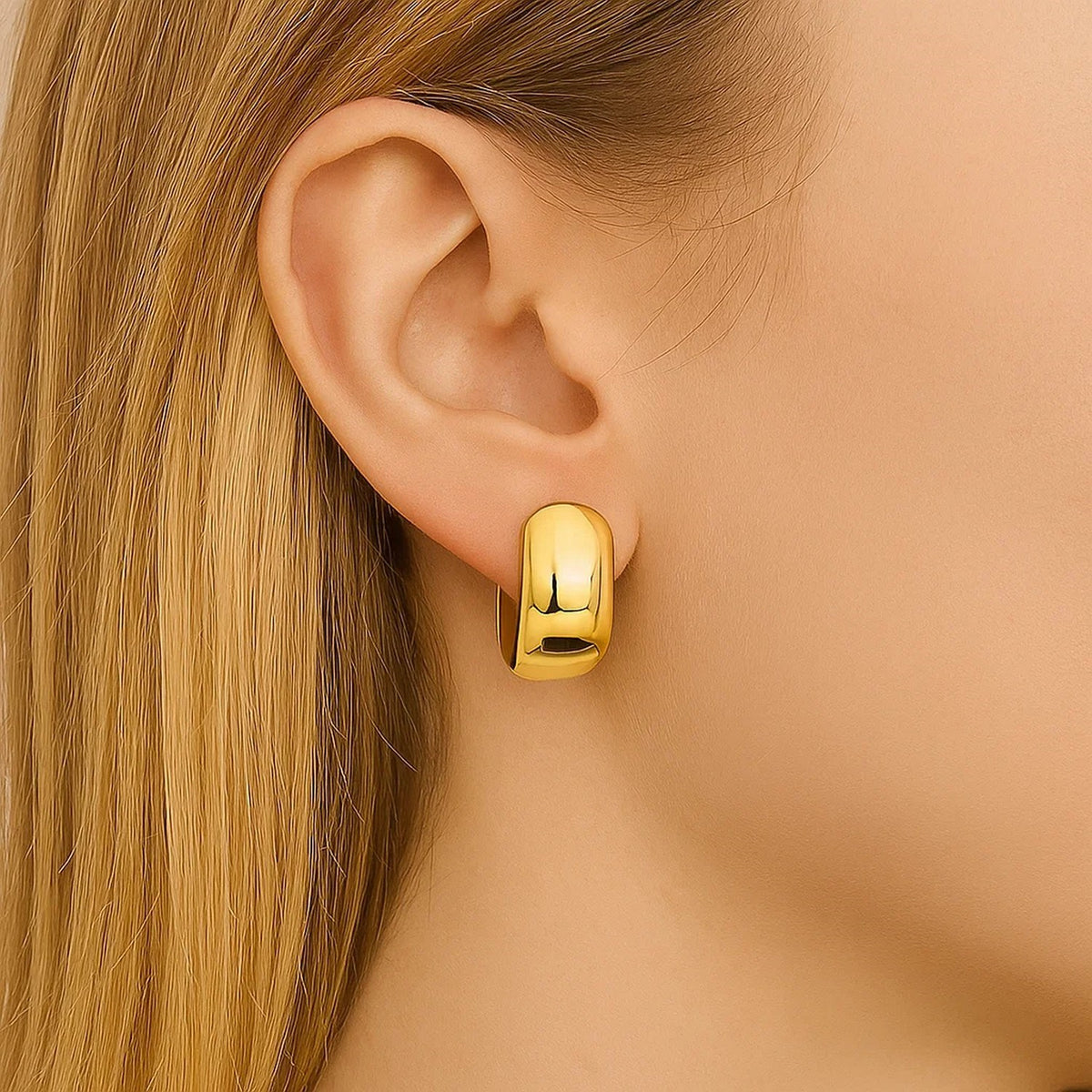 Close-up of a wide 14K yellow gold huggie on the ear