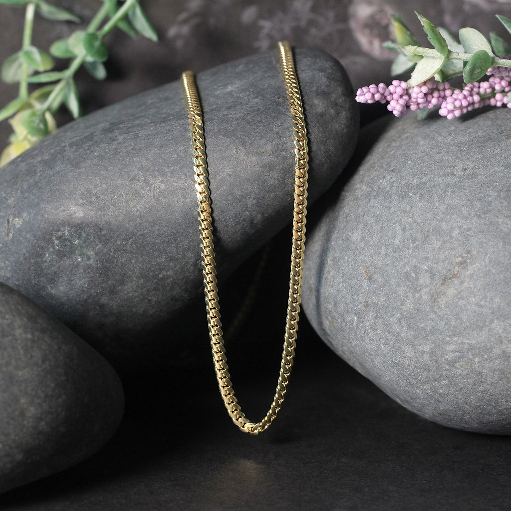 Solid Miami Cuban chain in 14K yellow gold draped over two stones
