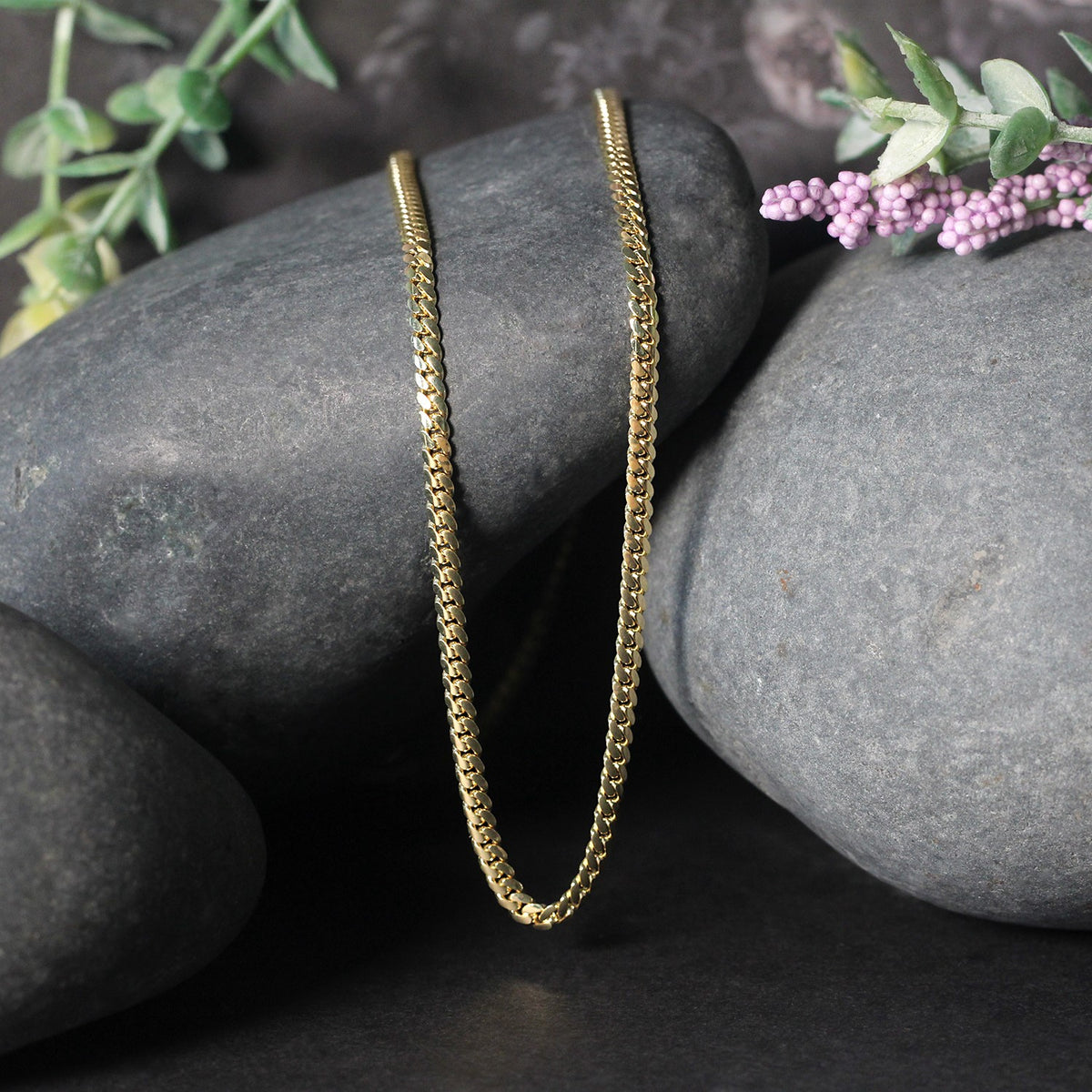 Solid Miami Cuban chain in 14K yellow gold draped over two stones