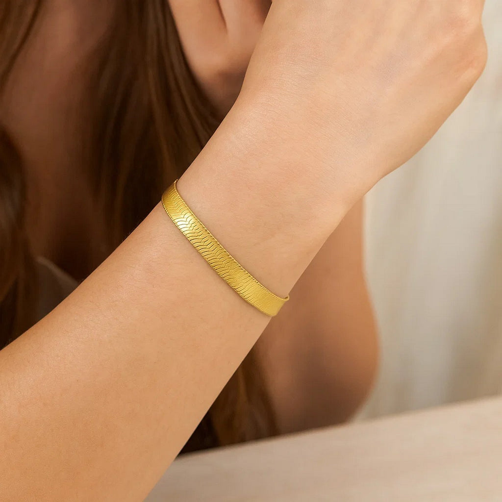 Flat yellow gold herringbone bracelet on a woman's raised wrist
