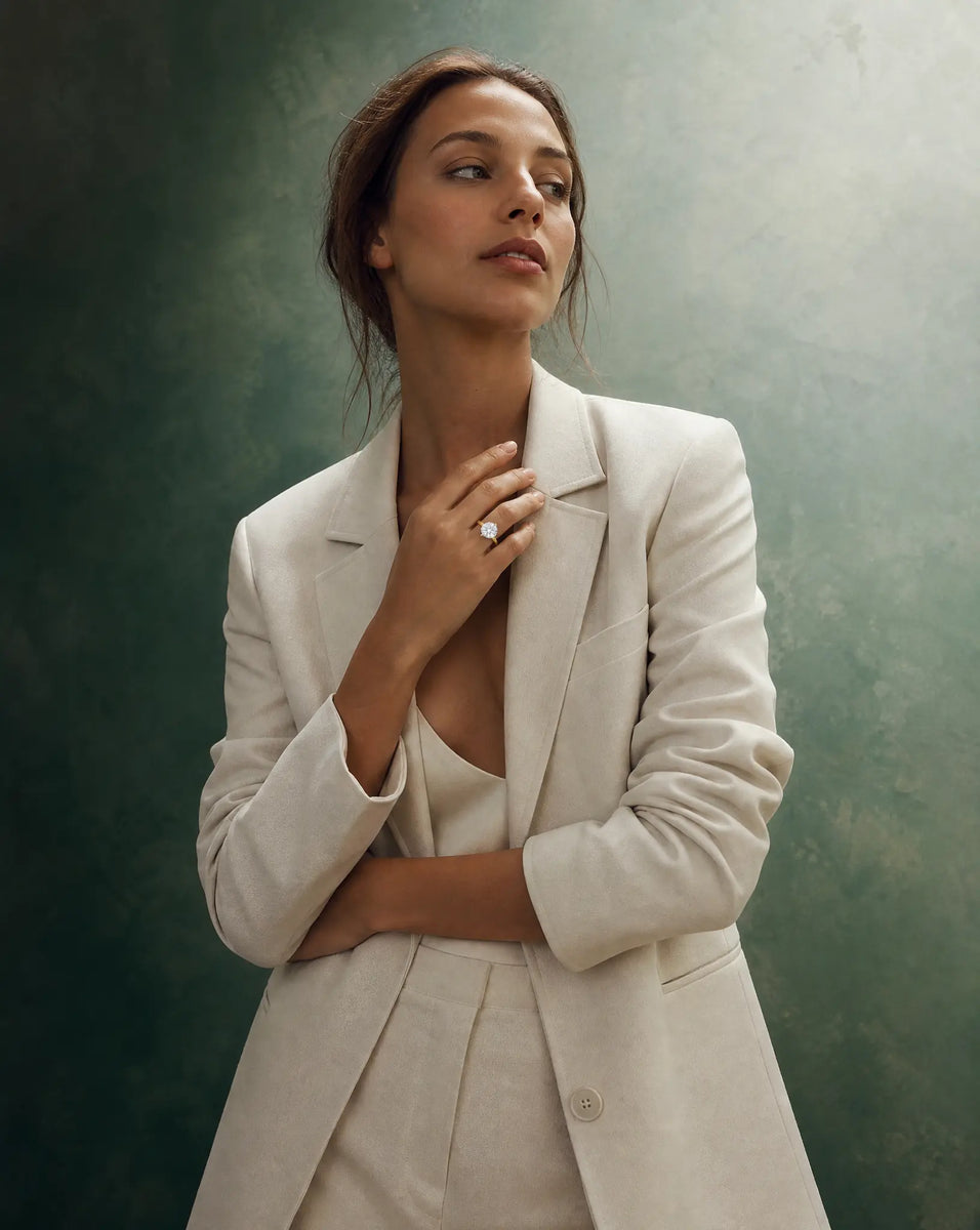 Woman wearing a beige suit against a textured green wall promoting a 5 carat IGI lab grown diamond ring from Deeve Canada in 14k gold