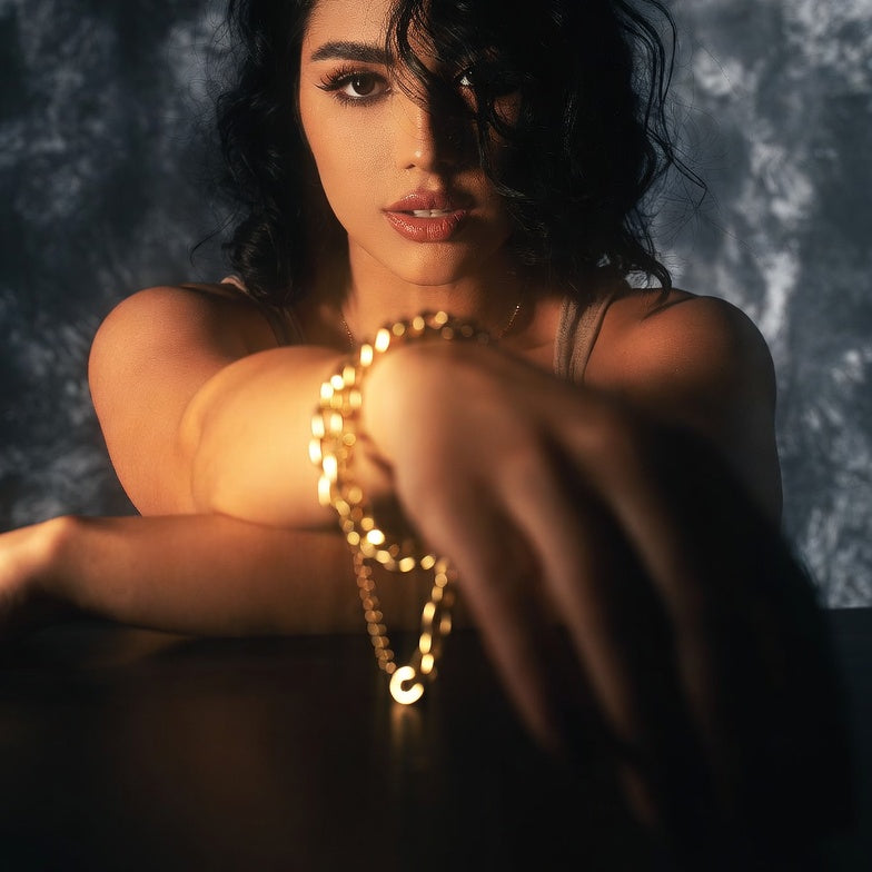 Woman with 14K cuban gold chain bracelet against a dark textured background