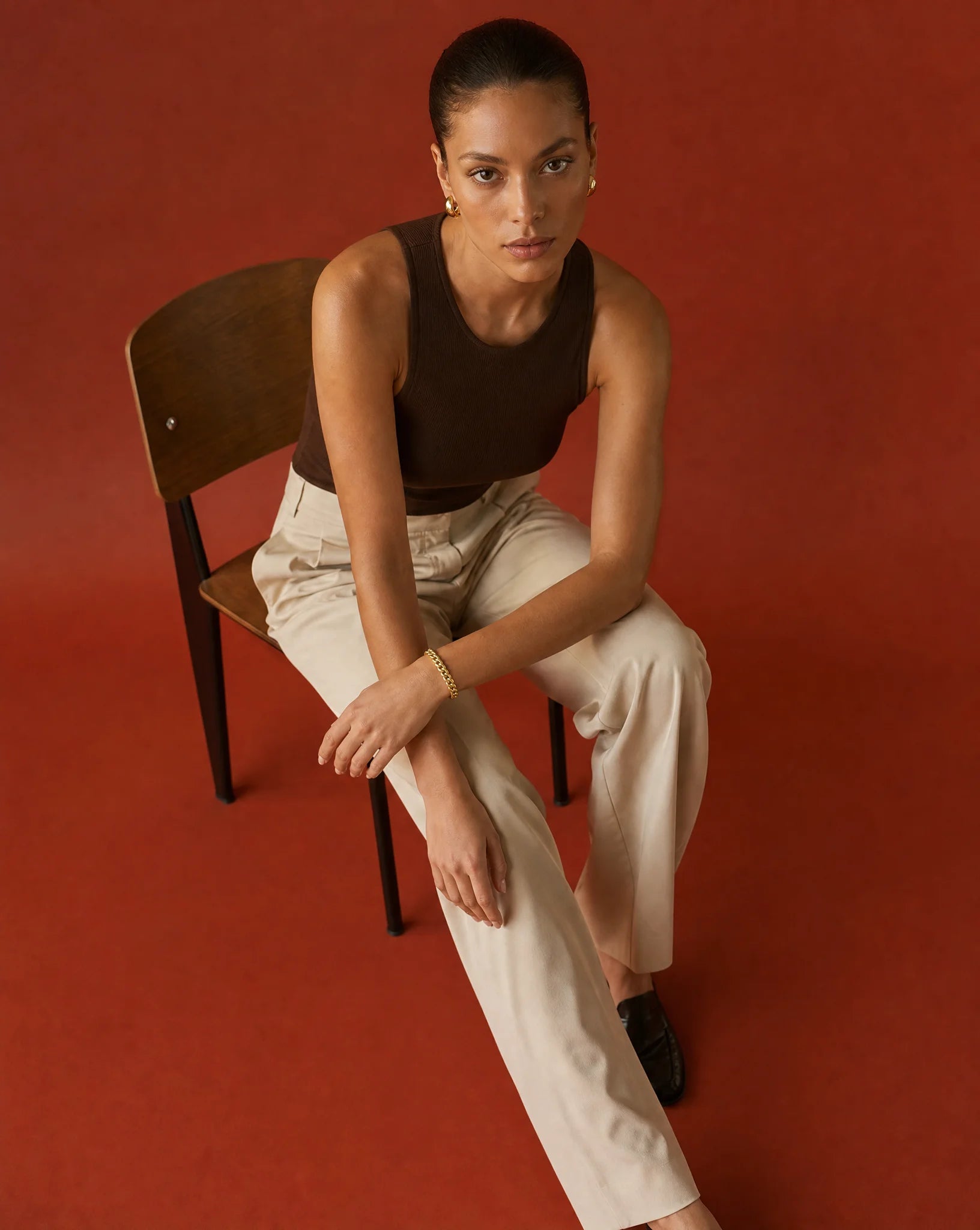 Woman sitting on a chair against a red background wearing 14k yellow gold cuban chain bracelet from Deeve Canada