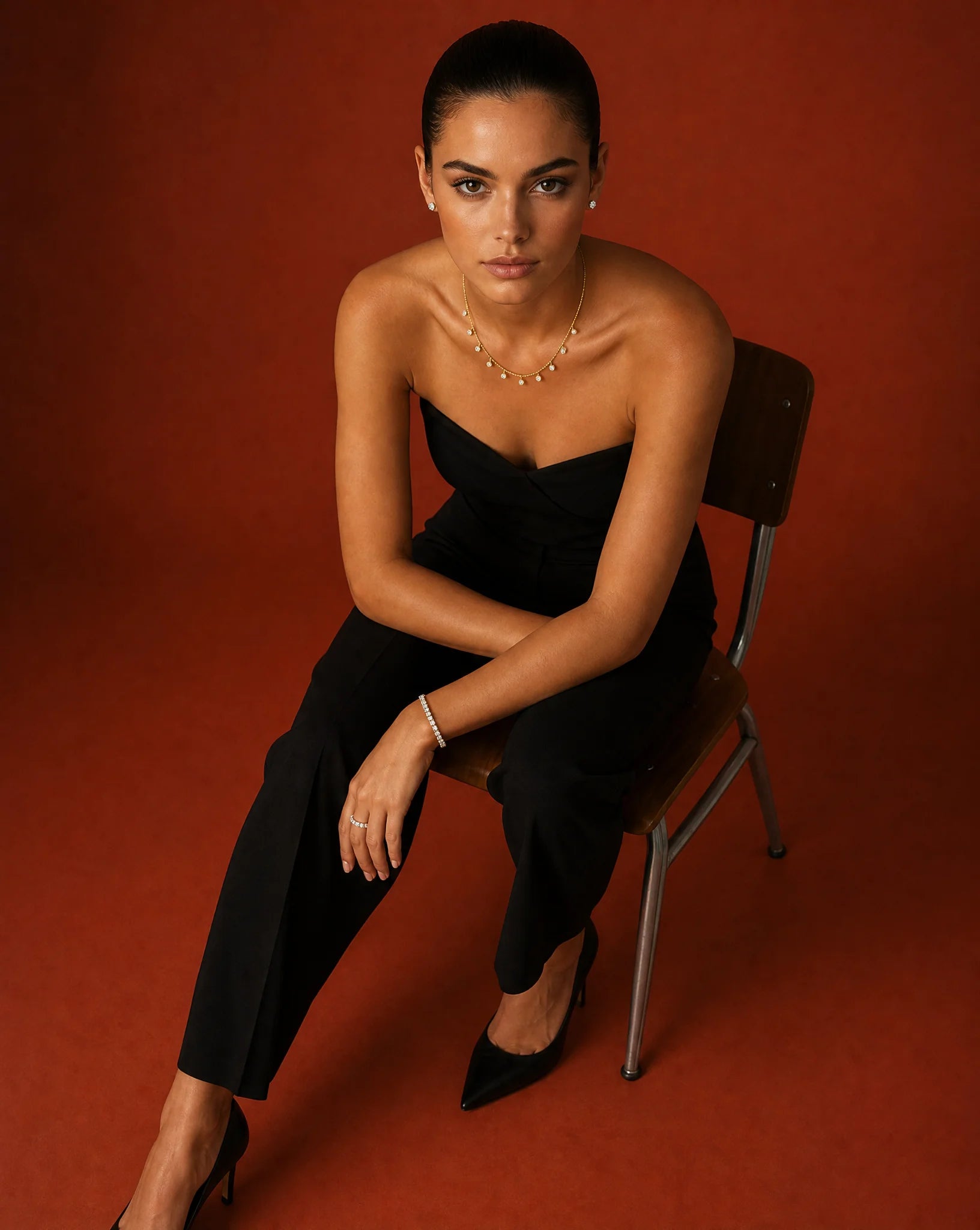 Deeve Canada's model promoting lab grown diamond jewelry collection in a black strapless jumpsuit sitting on a chair against a red background