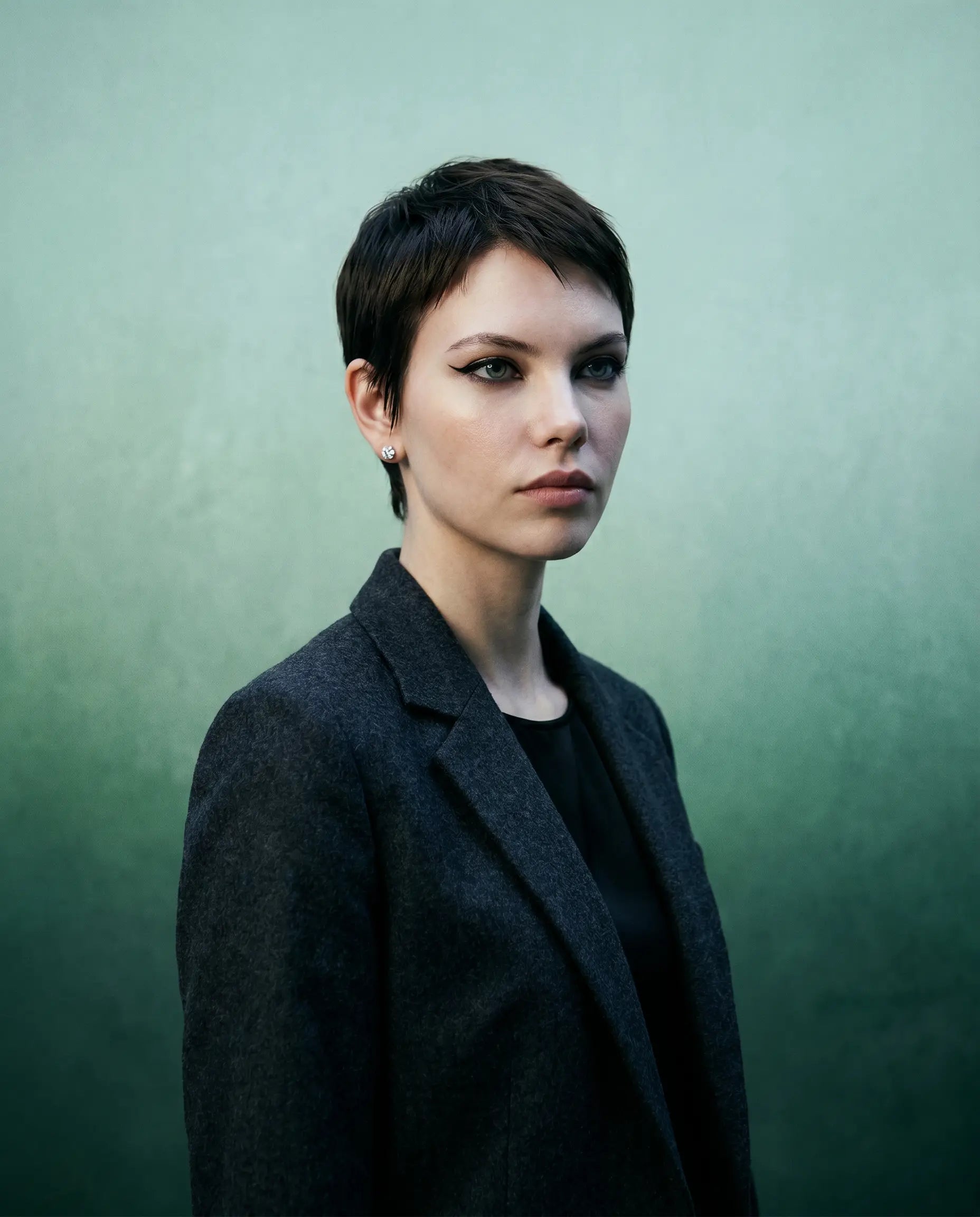 Deeve Canada model in short hair wearing a pair of 1 carat IGI certified lab grown diamond in 14k white gold wearing a dark coat against a green background