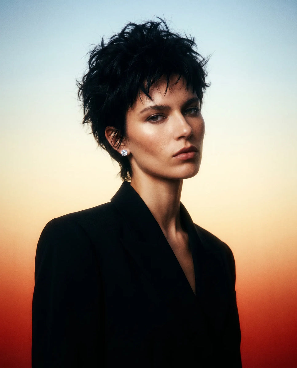 model with short dark hair wearing a black outfit waering 3 carat IGI certified lab grown diamond from Deeve Canada's diamond collection against a gradient sky background
