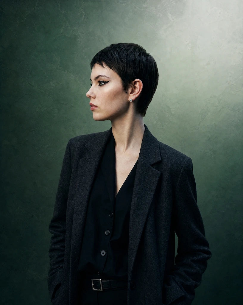 A model promoting IGI certified lab grown diamond stud earrings from Deeve Canada wearing a black suit against a green background