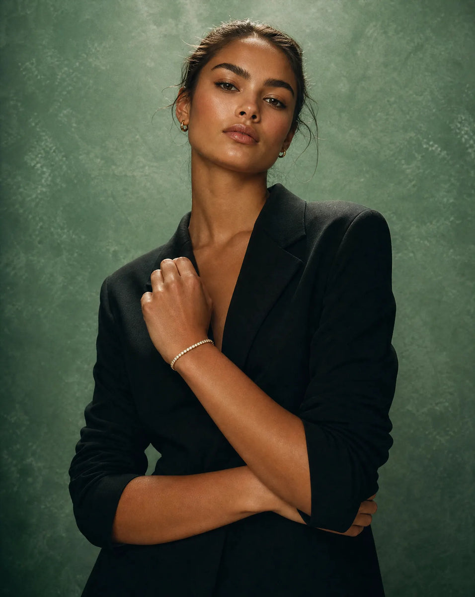 Woman wearing a black blazer against a textured green background promoting a 7 carat lab grown diamond tennis bracelet from Deeve Canada