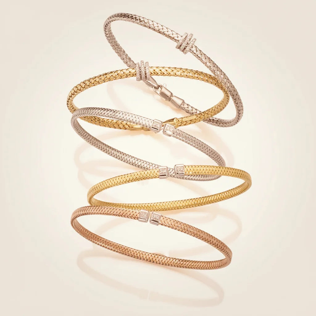 Three 14K gold bracelets of different designs from Deeve jewelry Canada on a light beige background