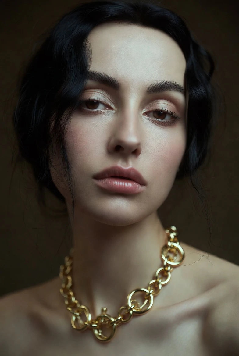 Woman wearing a 14K gold Cuban chain necklace from Deeve jewelry collection against a dark background